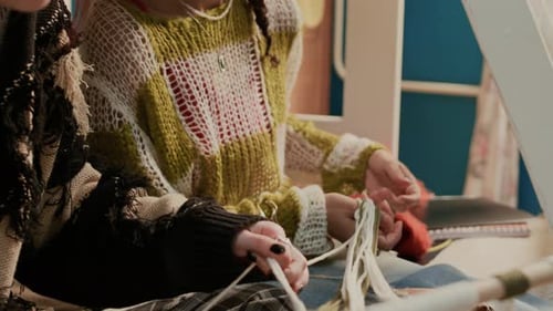 Female Roommates Stretching Threads of Macrame Piece Hanging on Wooden Stick