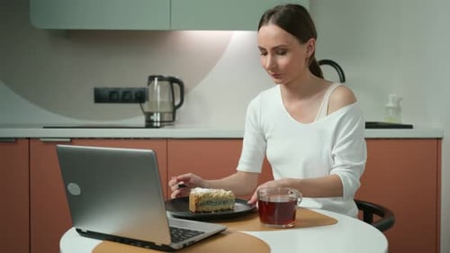 Young Woman Enjoys Cake and Laptop in Kitchen