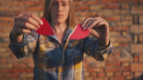 Woman Tearing Red Heart in Front of Brick Wall