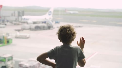 Child looking out window at airplane, while waiting for their airplane flight in transit hall near d