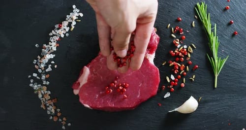 Beautiful juicy fresh meat steak on a table with salt, rosemary, garlic, and tomato on a black bac