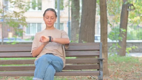 Woman Checks Smart Watch While Sitting on Bench