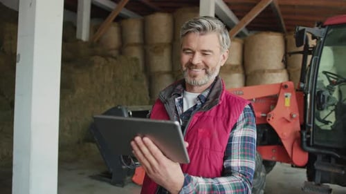 Farmer Using Tablet in Barn With Tractor