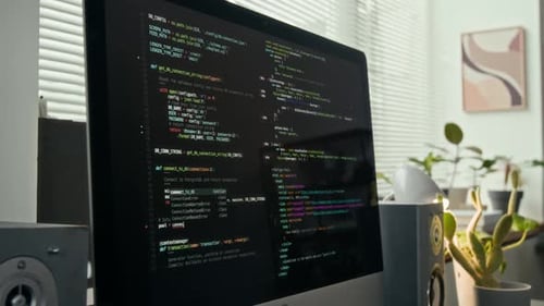 Computerbildschirm mit farbigem Programmiercode und zwei Desktop-Lautsprechern