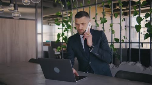 Male Businessman Working in a Modern Office at a Laptop and Calls on the Phone Portrait of a Male