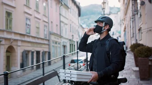 Delivery man with face mask delivers pizza in town during coronavirus pandemic