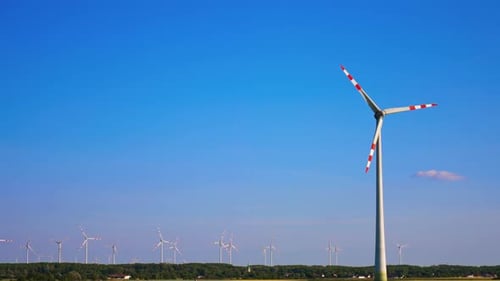 Tall wind turbine rotating in the blue clear sky. Wind farm in the fields at backdrop