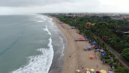 Sandy beach and foamy ocean waves with urban Bali coastline on moody day