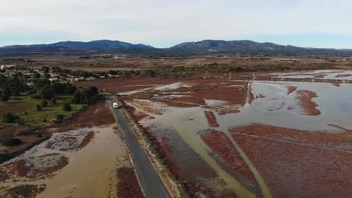 Aerial: truck and van going through a flat road among a marsh and some mountains in the background