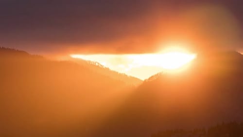 Sunlight Pierces Through Mountainous Tree Line