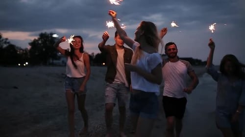 Amigos caminhando, dançando e se divertindo durante a festa noturna à beira-mar com luzes cintilantes de Bengala