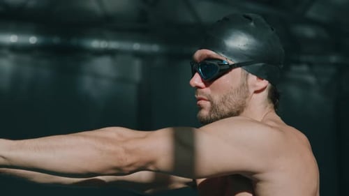 Muscular Swimmer in Cap and Goggles Doing Warmup Movements in Pool