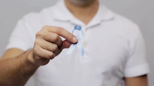 Man holds light blue prostate cancer awareness ribbon