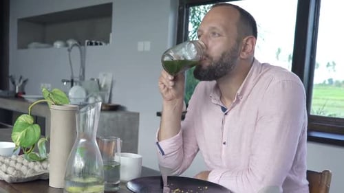 Bearded Man Drinking Green Smoothie at Wooden Table
