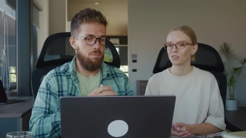Two Business Colleagues Engaging in Video Conference on Laptop in Bright Office Gesturing and
