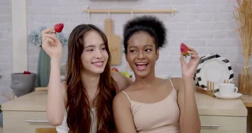 Two Young Women Sharing a Strawberry in Kitchen