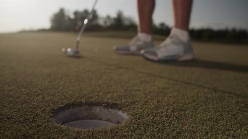 Golfer Sinks Ball Into Hole with Golf Club on Court at Sunset