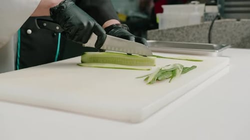 Close-up of a sushi maker in gloves cutting a cucumber with a professional kitchen knife