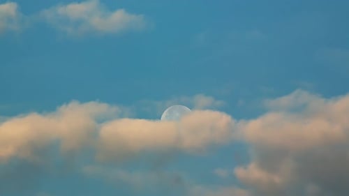Moon Drifting Behind Clouds in Blue Sky
