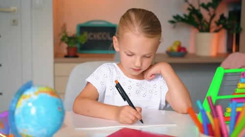 Child Kid Girl doing her homework art a desk. School girl writes in a notebook.