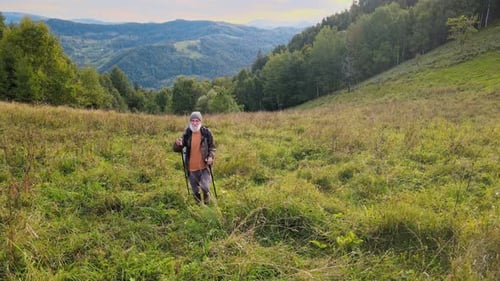 Elderly Man with a Backpack and Nordic Walking Sticks is Walking