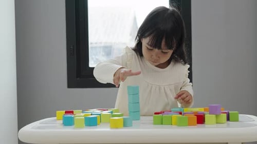 menina brincando de bloco para empilhar cubos de construção em uma mesa