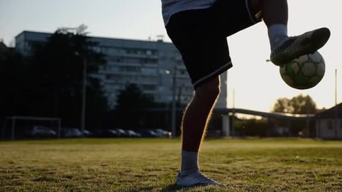 Jogador de futebol profissional fazendo malabarismos com bola de futebol no estádio ao pôr do sol Jovem chutando bola no verde