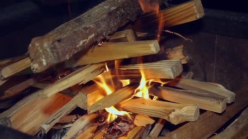 Firewood stacked in hot camp fire begin to burn on dark black night