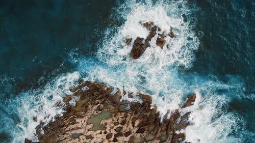 Ocean waves swirl and crash around rocky islands in a dramatic aerial perspective
