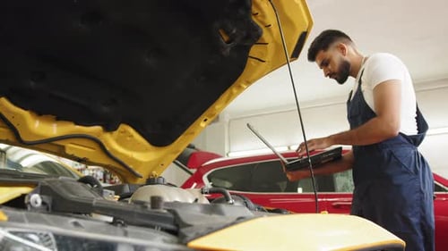 Der junge Automechaniker wartet das Fahrzeug mit einem Diagnose-Laptop-Computer für