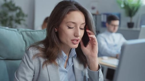 In Office Young Businesswoman Speaks on Phone Working on Laptop Computer On Background People