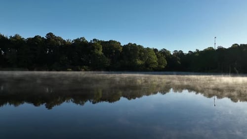 Aerial View of Calm Lake at Sunrise with Thin Layer of Fog and Clear Reflections Beneath Blue Sky