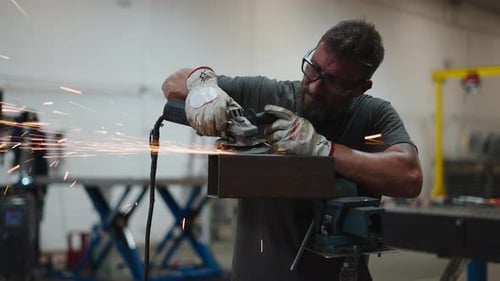 Konzentrierter männlicher Arbeiter, der in einer Werkstatt mit einem Winkelschleifer an einem Metallprofil Funken erzeugt
