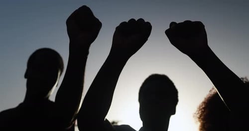 People with Raised Fists Silhouetted Against Sky
