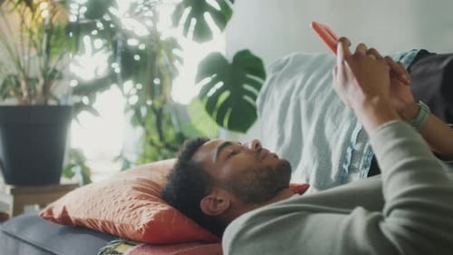 Mann liegt auf der Couch und schreibt SMS am Telefon