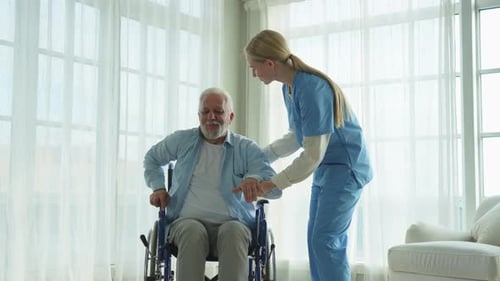 Rehabilitation Healthcare Physiotherapist Nurse Helps Old Man Patient in Wheelchair Stand Up Walking