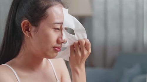 Close Up Of Beautiful Young Asian Woman Taking Off Sheet Facial Mask, Touching Her Face