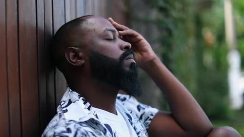 Pensive Man with Beard Leans Against Wall Outdoors
