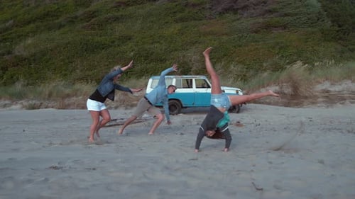 Friends cartwheeling and posing on a beach near car