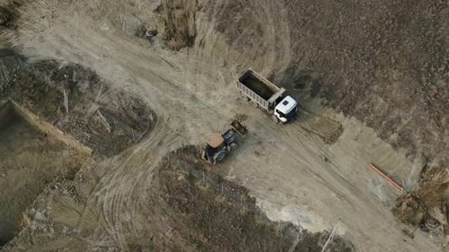 Luftbild eines gelben Traktors mit einem Eimer voller Erde, der Aushubarbeiten durchführt und gießt