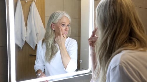 Woman Applying Face Lotion in Bathroom Mirror
