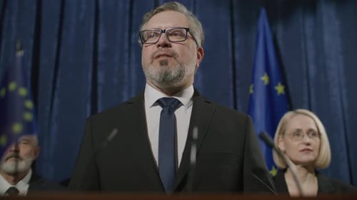 Man Speaks at Podium with EU Flags