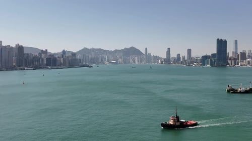 Hong Kong cityscape seen from cruise ship leaving the city. Tug boat on calm water with China landsc