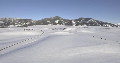 Luftflug in Richtung Berge entlang eines großen verschneiten Feldes
