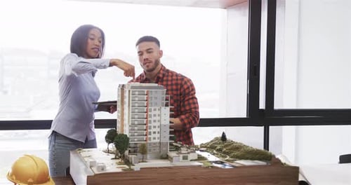 Diverse male and female architect discussing architectural model in office, slow motion