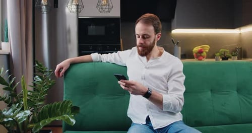 Young Man Relaxing on Couch Using Smartphone