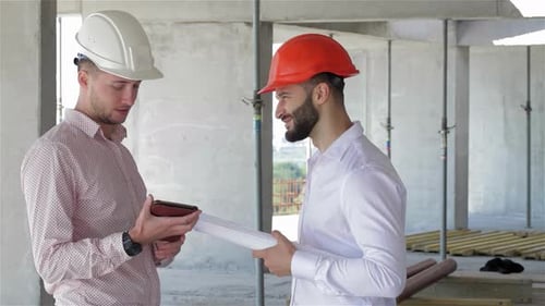 Two Builders Engaged in a Lively Discussion Over a Digital Tablet at a Construction Site