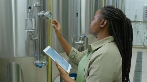 Black Brewery Technician Checking Gauge and Completing Checklist