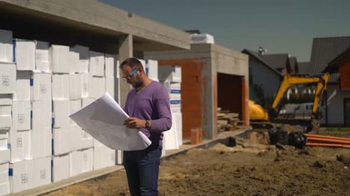 Young Man Reading Blueprints and Checking New House 30s