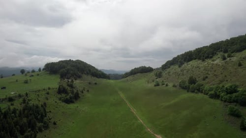 Lush green hills under a cloudy sky, aerial view of a serene landscape
